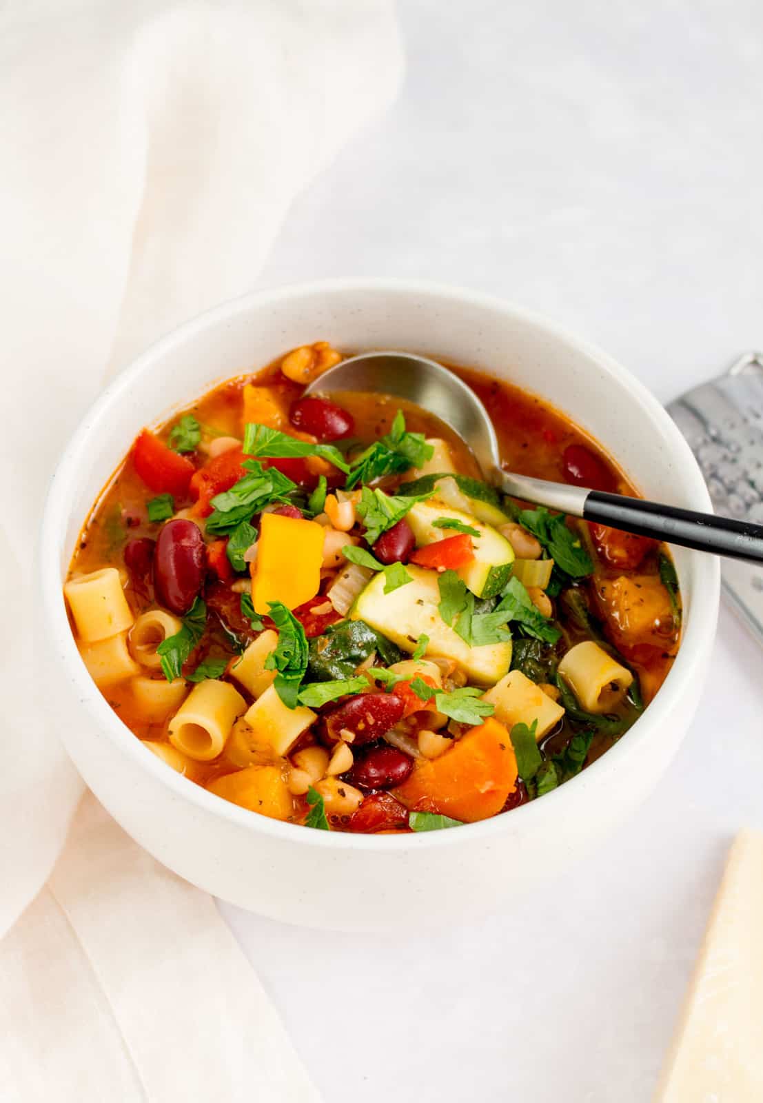 A white bowl with vegetarian minestrone with a spoon inside.