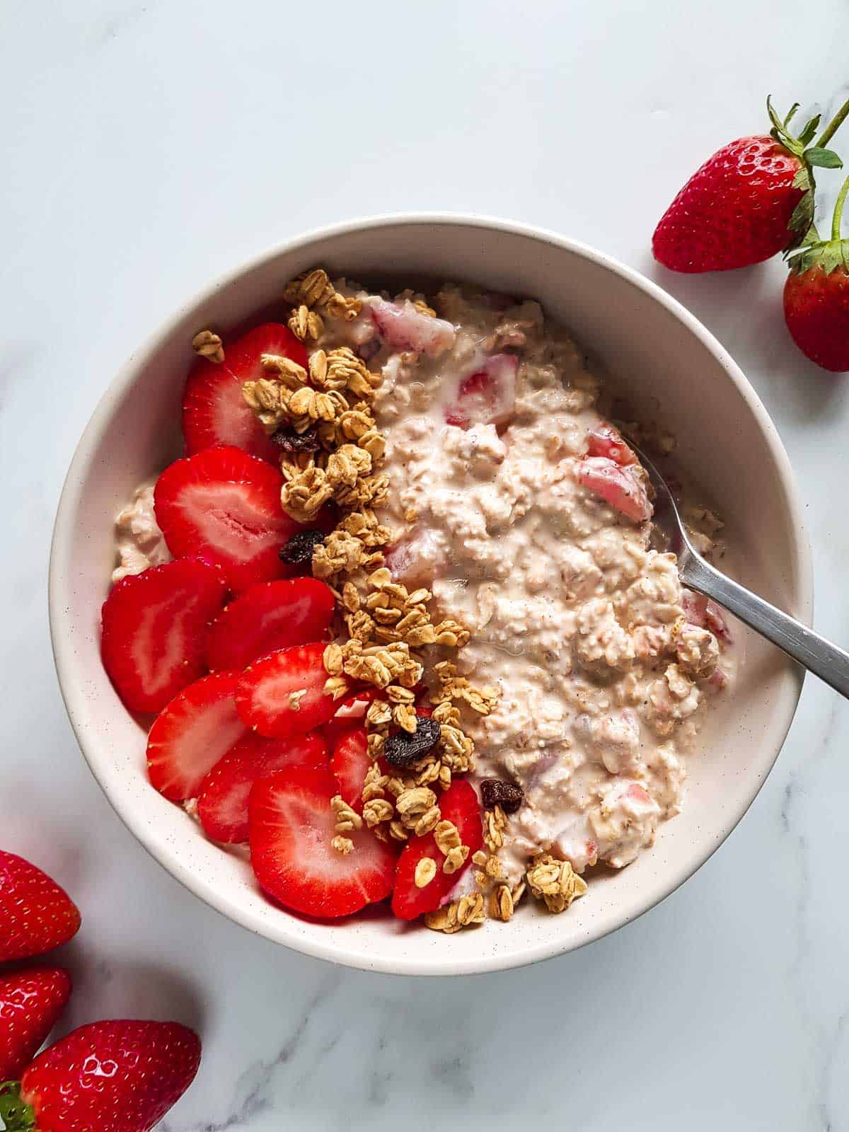 A bowl of strawberry overnight oats topped with strawberries and granola.