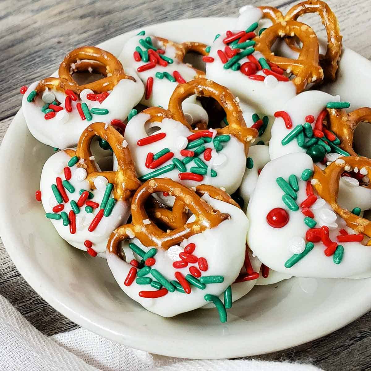 Overhead view of Christmas pretzels on a white plate sitting on a weathered wooden table.