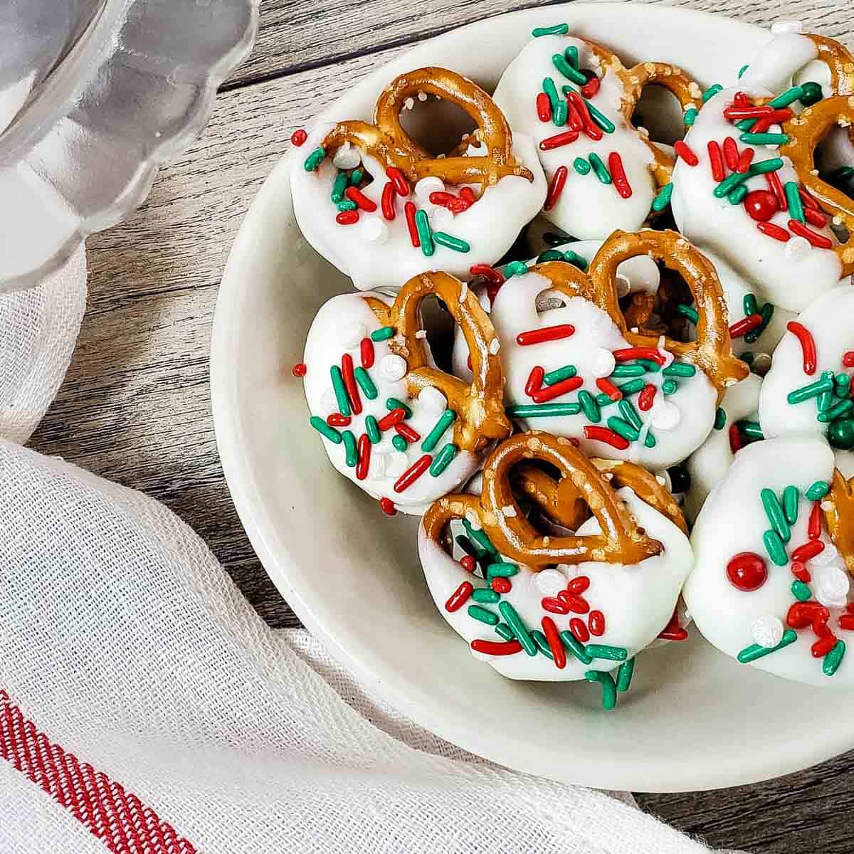 Christmas pretzels garnished with holiday sprinkles on a white plate.