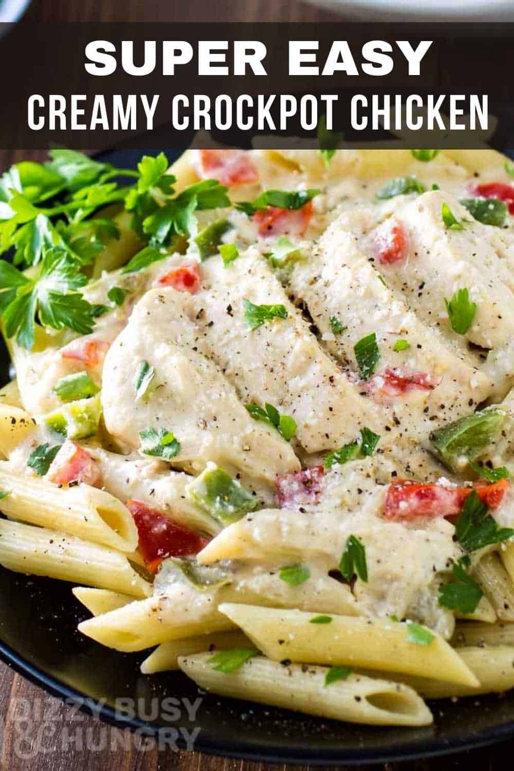 Close up view of creamy crockpot chicken on penne on a black plate with herbs on the side.