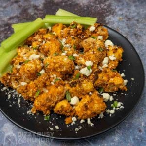 Side view of buffalo cauliflower sprinkled with cheese crumbles and herbs with celery on the side.