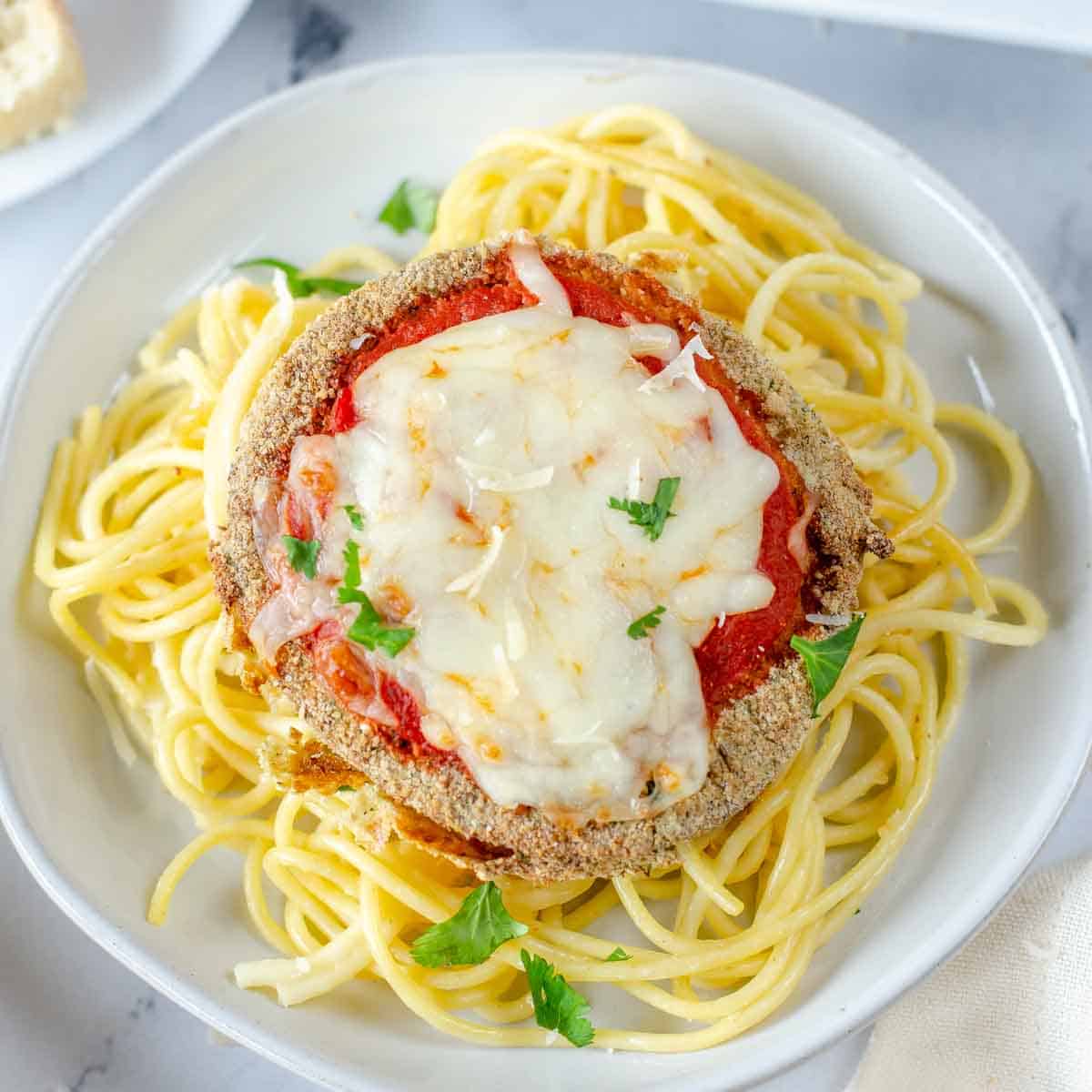 Beautifully air fried eggplant parmesan round over a bed of spaghetti topped with chopped parsley.