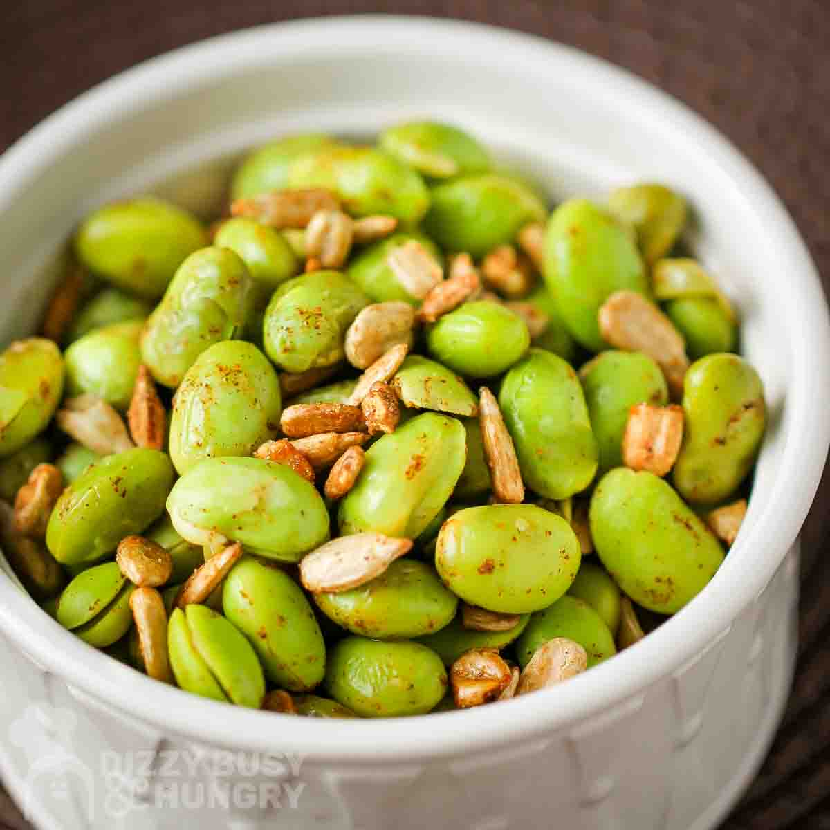 Side view of chipotle edamame in a white bowl with a brown background.