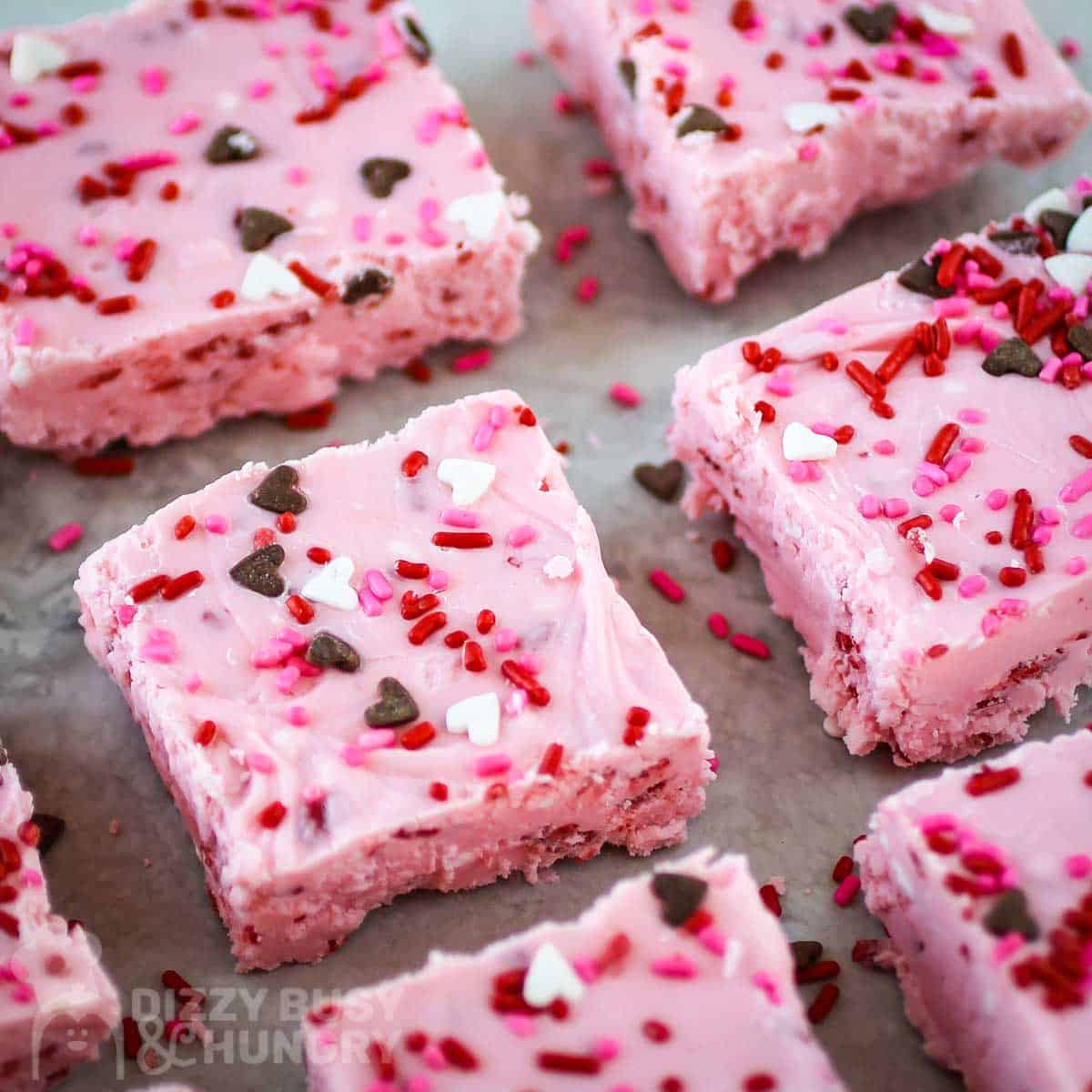 Overhead shot of pieces of strawberry fudge spread out on parchment paper garnished with sprinkles.