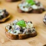 Close up shot of one sweet potato slice garnished with basil on a wooden cutting board with more in the background.