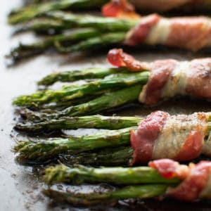 Close up image of bacon wrapped aspargus on a baking sheet.