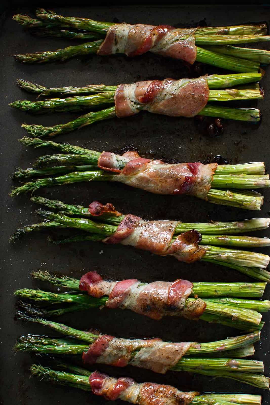 Oven baked bacon wrapped asparagus on a baking sheet.