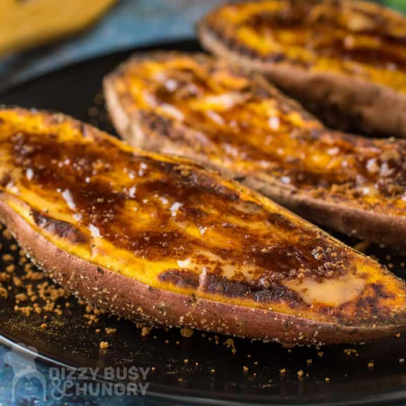 Super close up view of the finished sweet potato half on a black plate with two more halves in the background.