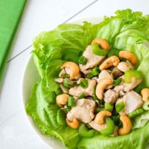 Close up shot of lettuce wrap garnished with cashews and scallions on a white plate with a green cloth on the side.