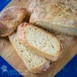 Overhead shot of half of the bread loaf with some slices on a wooden cutting board with a blue background.