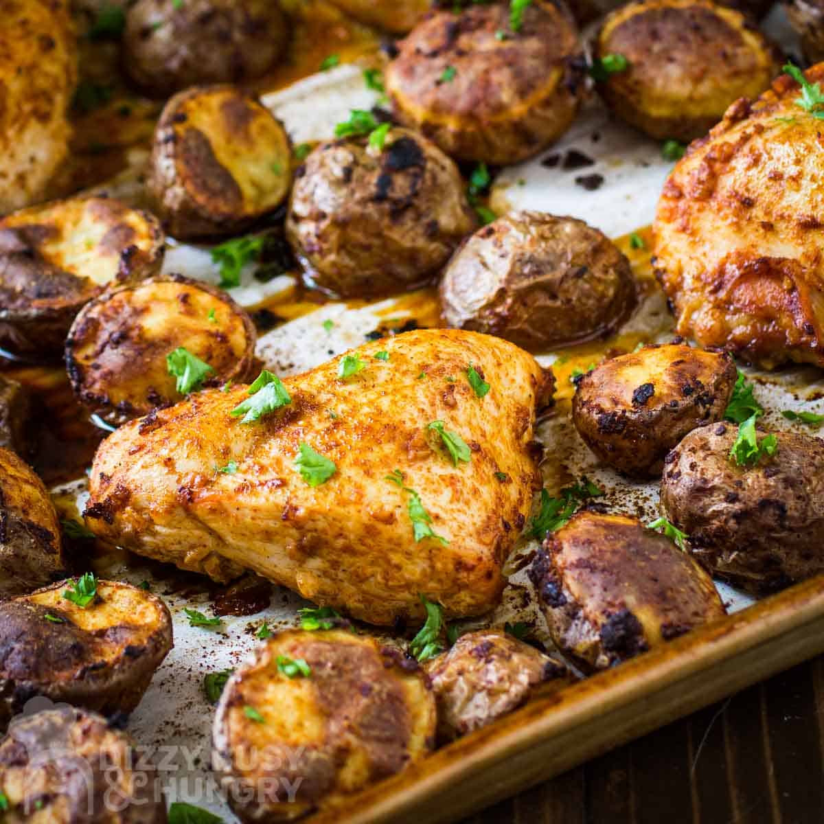 Side close up shot of chicken tray bake on a baking sheet lined with parchment paper garnished with herbs.