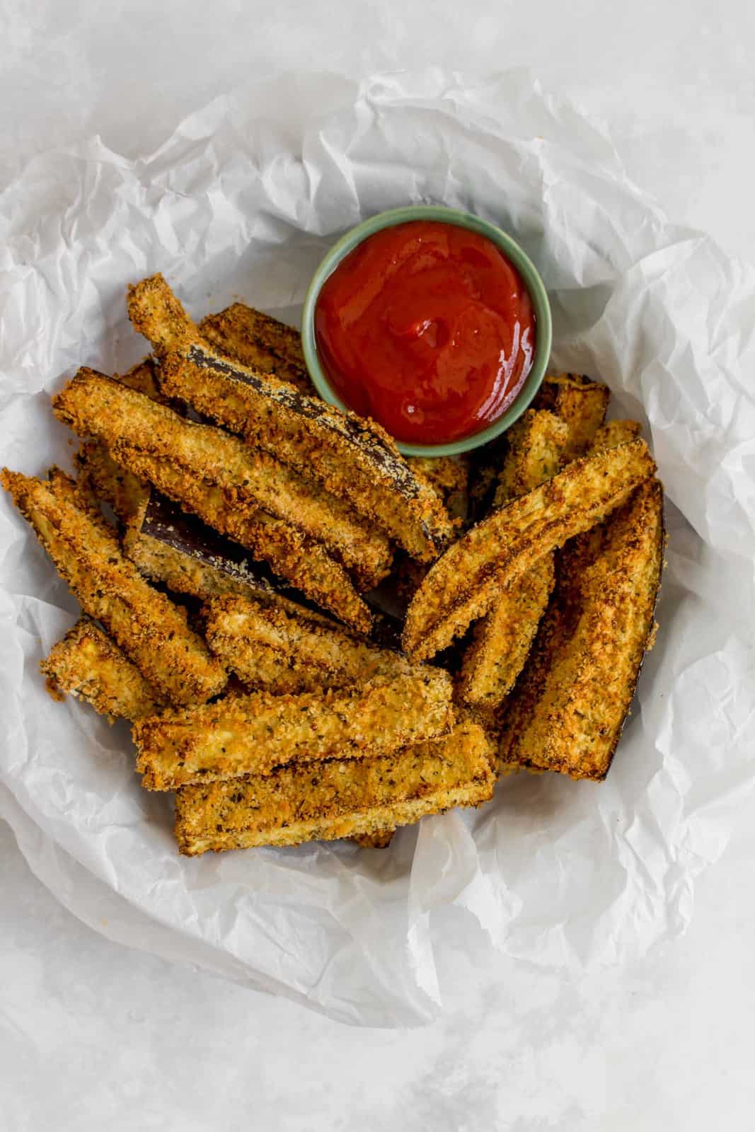 A plate with parchment paper, containing air fryer eggplant fries and dip.