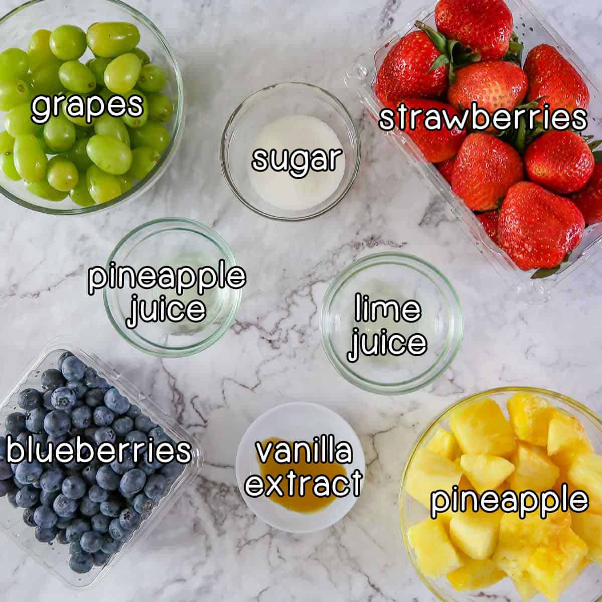 Overhead shot of ingredients- strawberries, grapes, blueberries, pineapple, sugar, pineapple juice, lime juice, and vanilla extract.