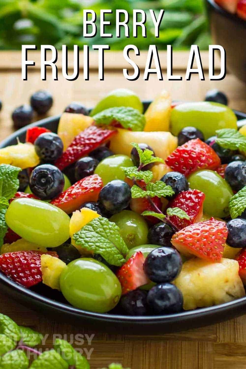 Side view of berry fruit salad with a mint garnish on a black plate on a wooden surface.