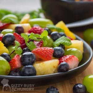 Side shot of berry fruit salad with a mint garnish on a black plate.