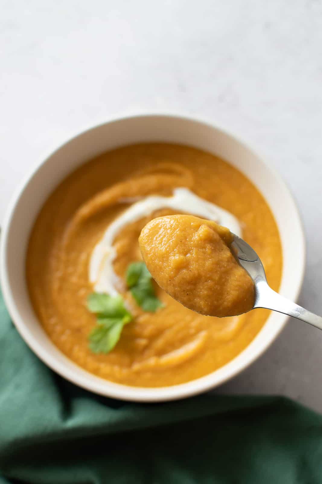 A spoon with carrot soup hovering above a bowl of soup.