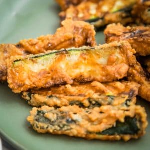 Side close up shot of multiple zucchini fries on a light green plate with a white background.