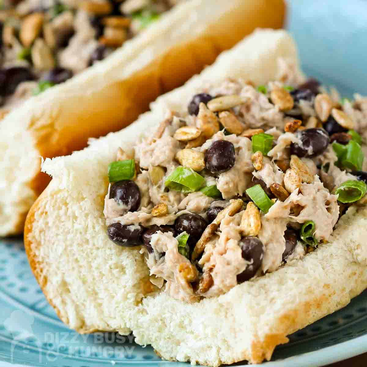 Close up side view of tuna salad sandwich garnished with herbs on a light blue plate.