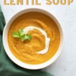 Carrot and lentil soup in a white bowl with a green cloth.