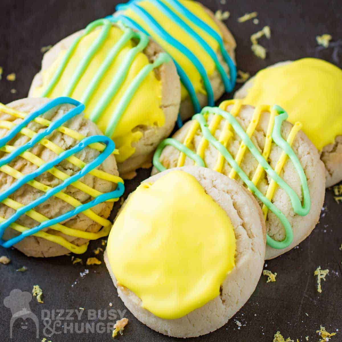 Side close up shot of six lemon cookies with blue, yellow, and blue icing on a brown surface.