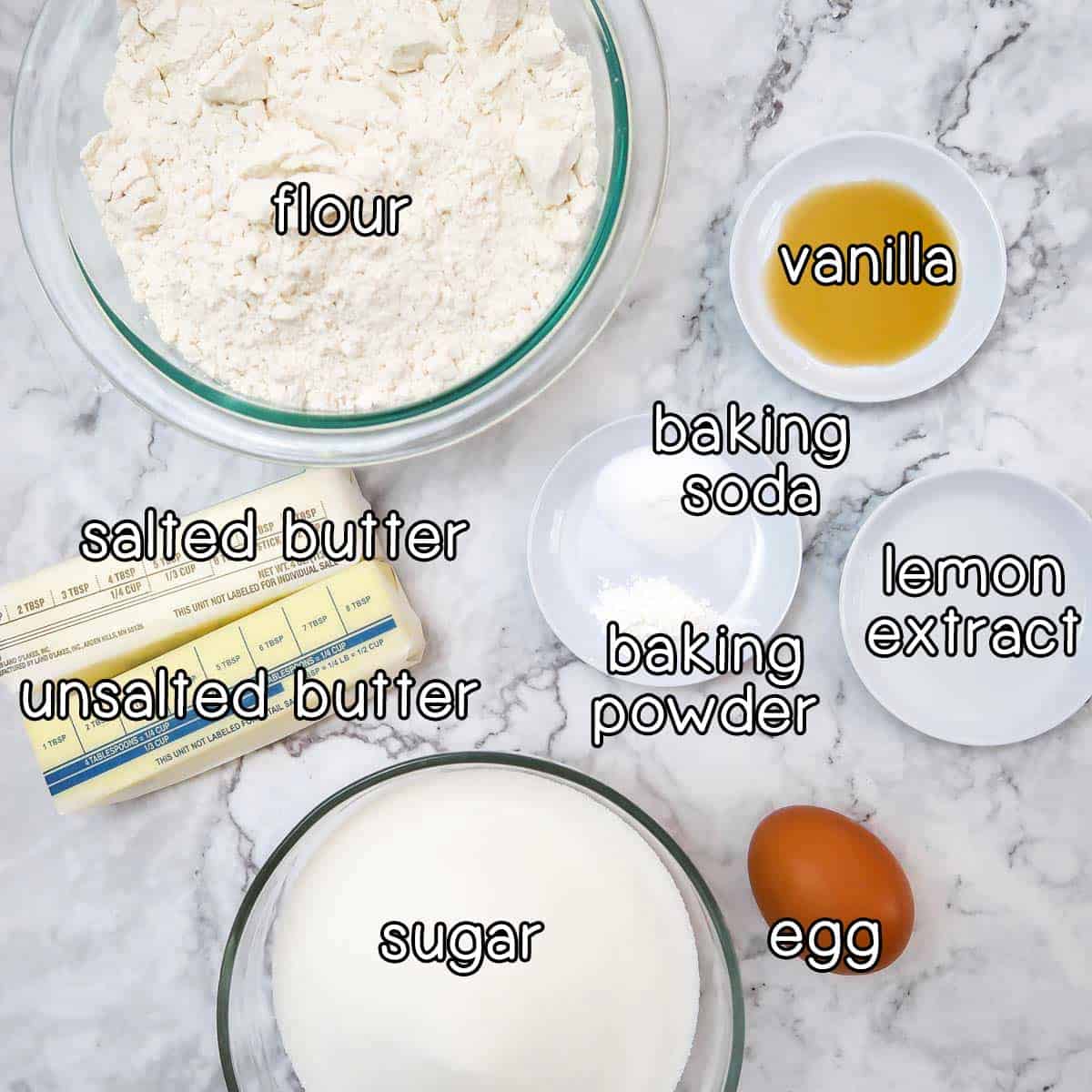 Overhead shot of cookie ingredients- flour, vanilla, baking soda, baking powder, lemon extract, an egg, sugar, salted butter, and unsalted butter.