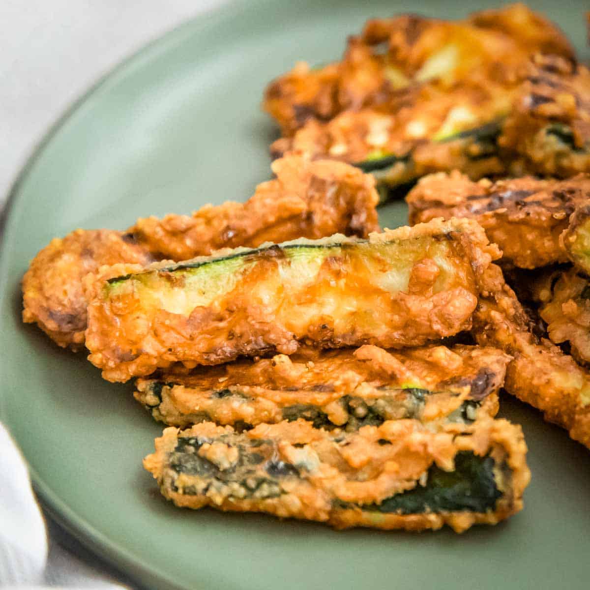 Side close up shot of multiple zucchini fries on a light green plate with a white background.