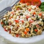 Side angled view of ground beef orzo pasta in a white bowl with a fork on the side.