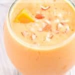 Overhead shot of mango lassi in a clear curvy glass garnished with mango chunks and pieces of almonds.