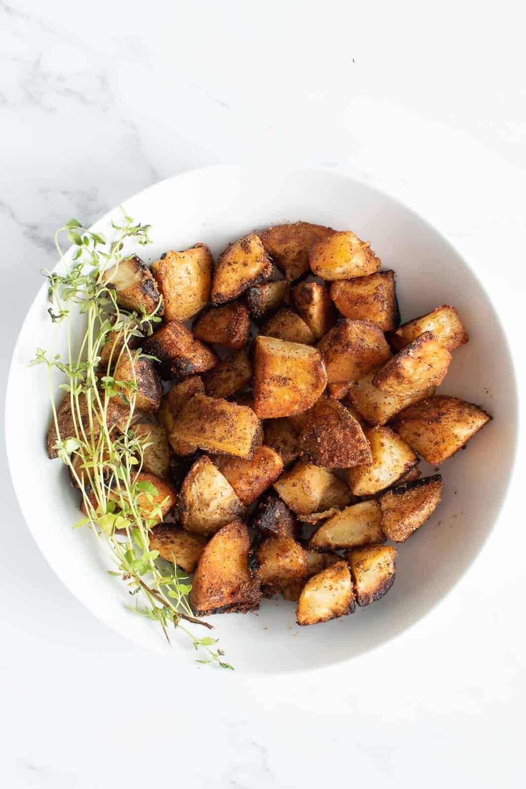 A bowl of crispy diced potatoes with thyme on the side.