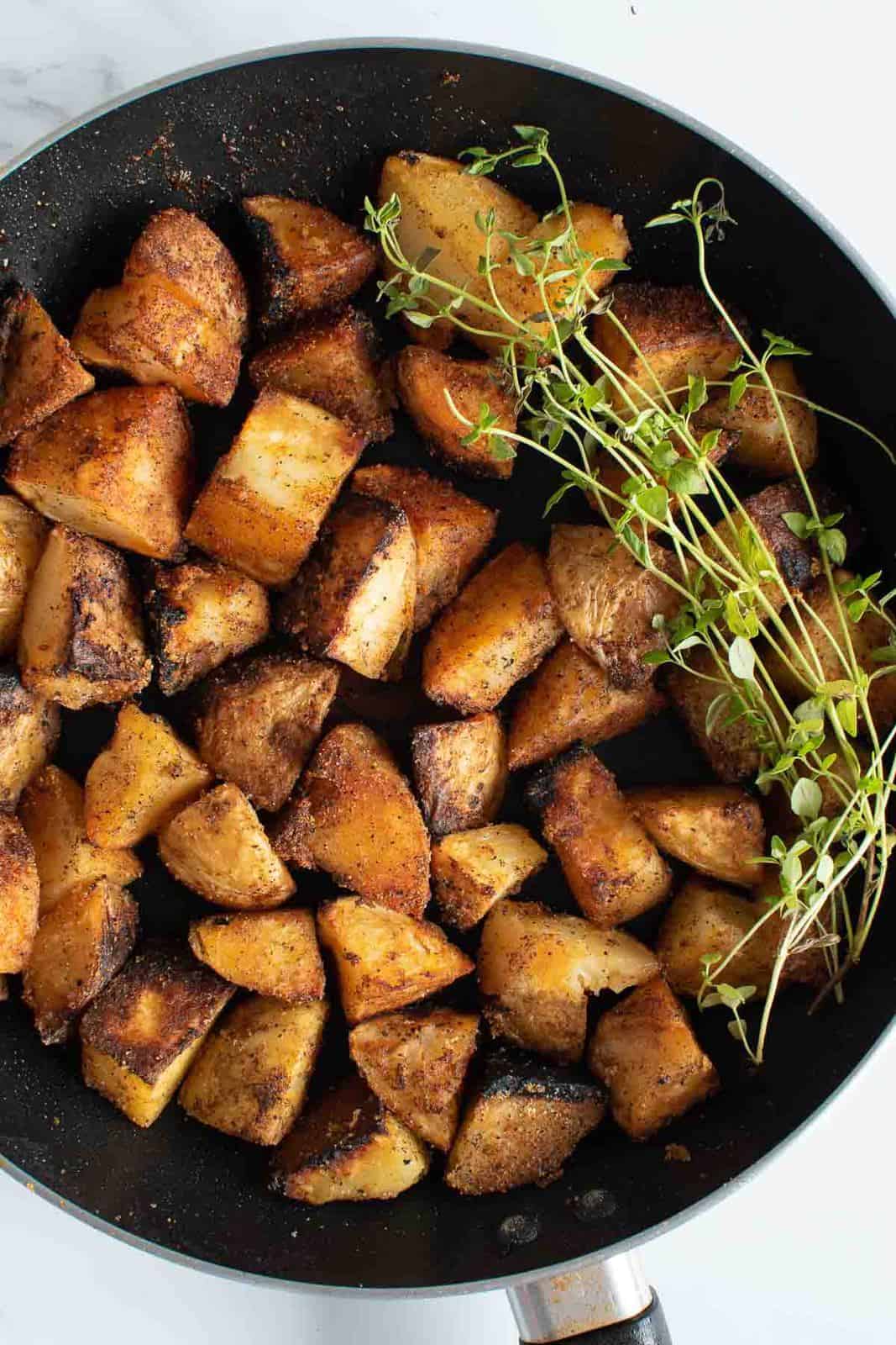 Golden sauteed potatoes in a frying pan, with fresh thyme on the side.