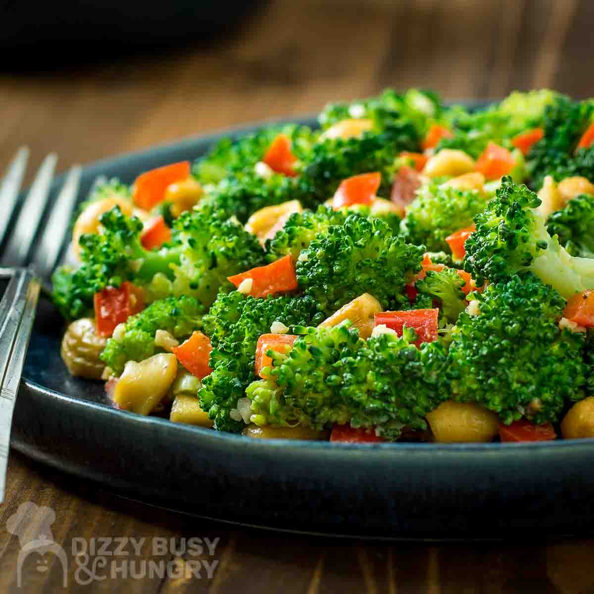 Side view of garlic butter broccoli in a blue bowl on a wooden surface with a fork on the side.