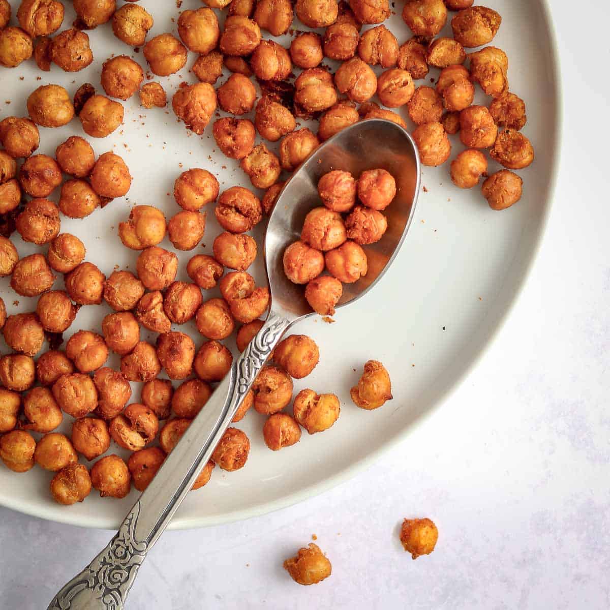 Overhead shot of crispy chickpeas on a white plate with a spoon holding some chickpeas on the side.