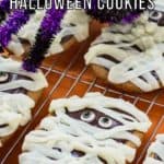 Side close up shot of multiple mummy cookies on a cooling rack with a purple and black decorative spider in the background.