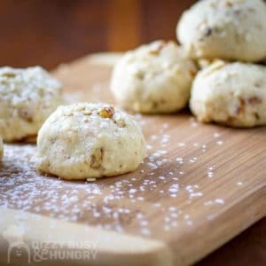 Side close up shot of a sesame cookie garnished with powdered sugar on a wooden cutting board with more cookies in the background.