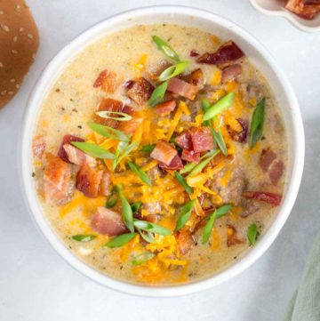 A bowl of instant pot cheeseburger soup with cheese, bacon, and green onions on top.