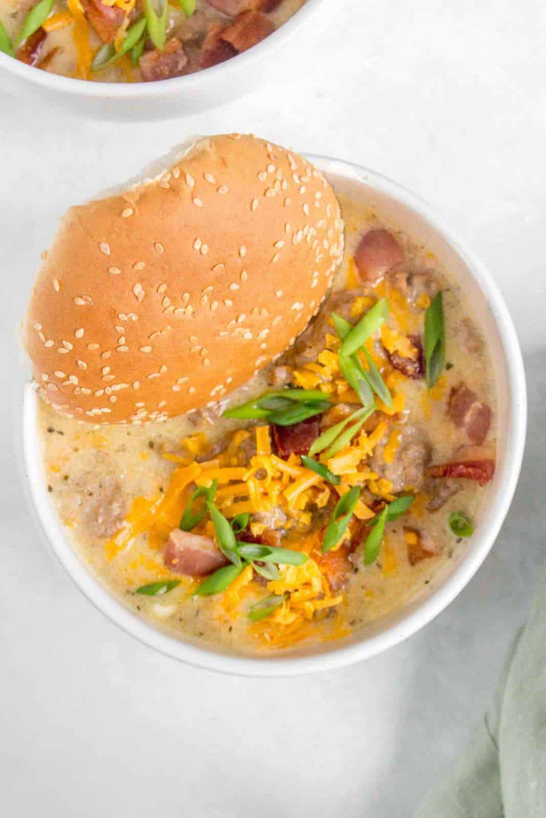 A bowl of instant pot cheeseburger soup with a burger bun.