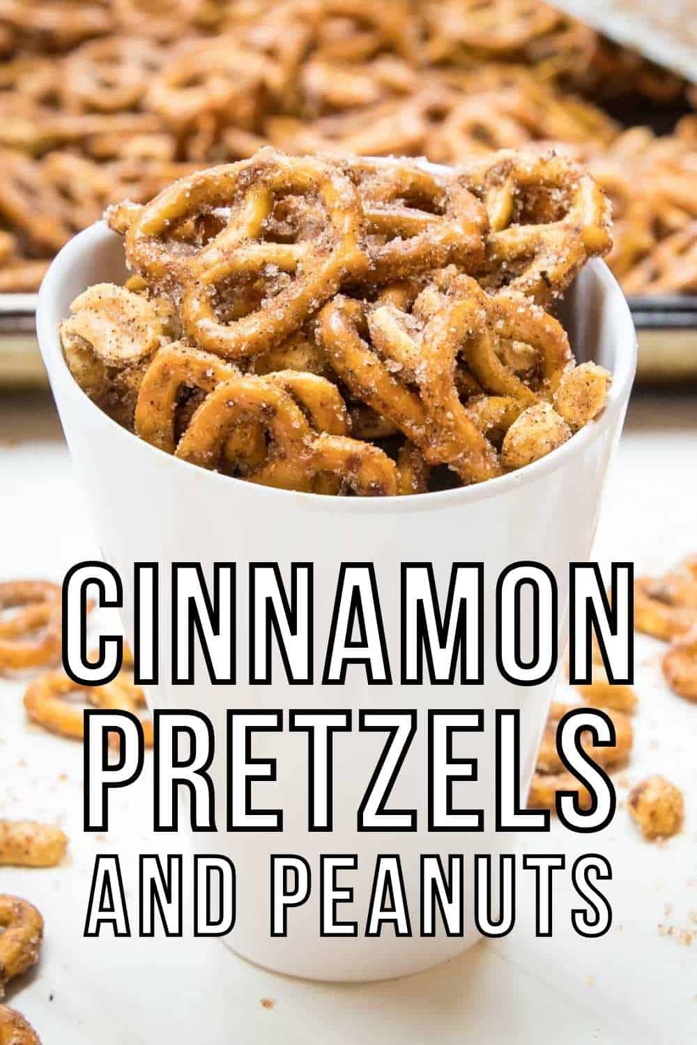 Side angled view of cinnamon pretzels in a white ceramic cup with more pretzels in the background on a baking sheet and scattered on a white surface.