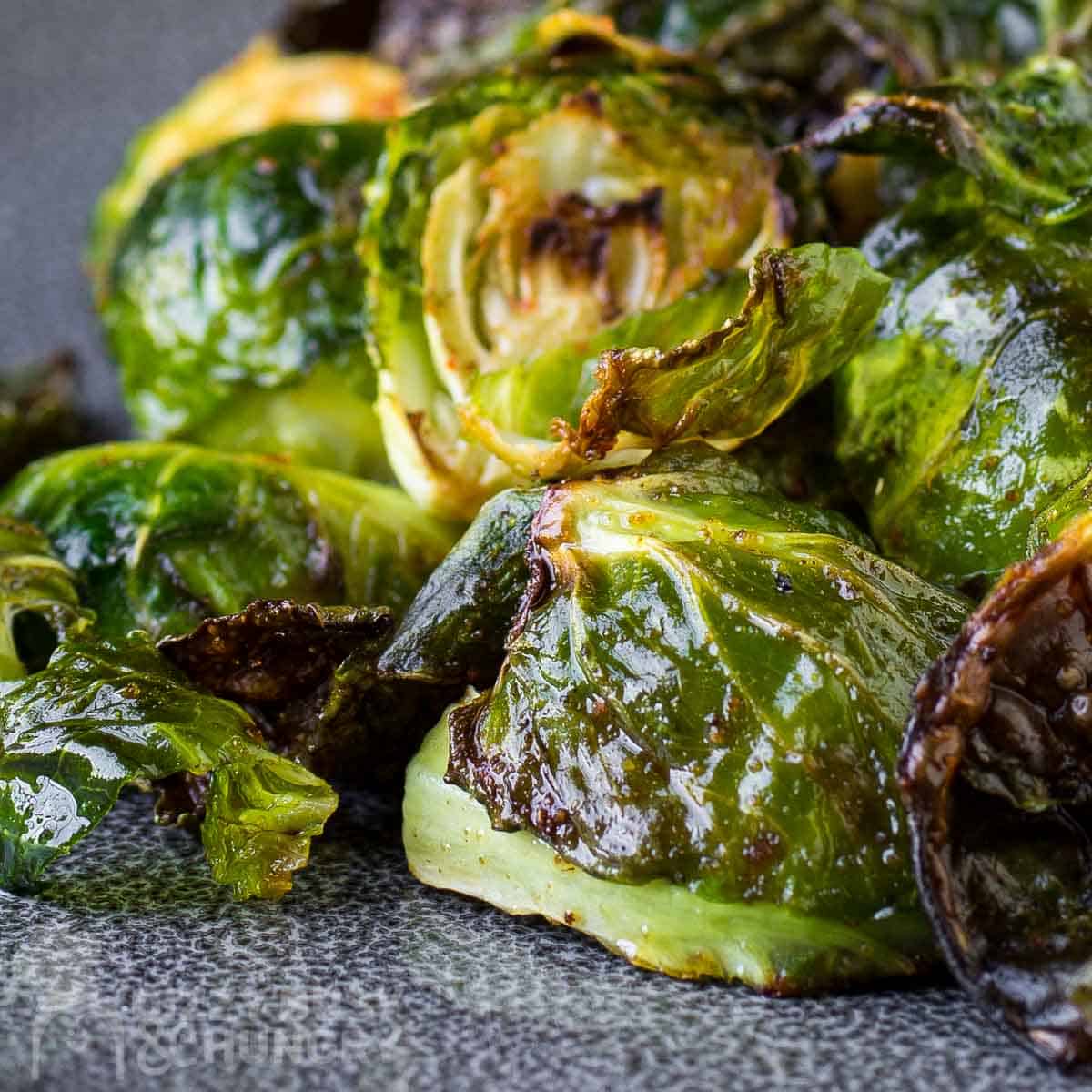 Close up view of garlic roasted Brussel sprouts on a blue and grey plate.