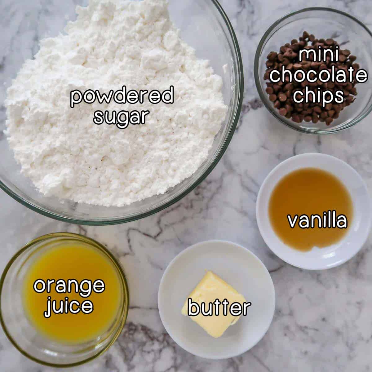 Overhead shot of ingredients for orange glaze- powdered sugar, mini chocolate chips, vanilla, butter, and orange juice.