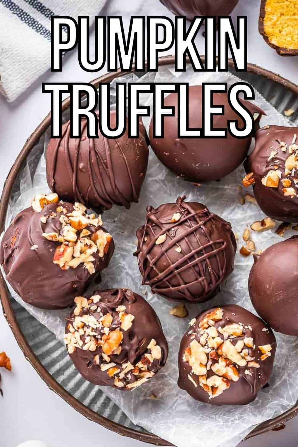 Overhead shot of multiple truffles, some decorated with pecans, on a brown plate lined with parchment paper on a white surface.