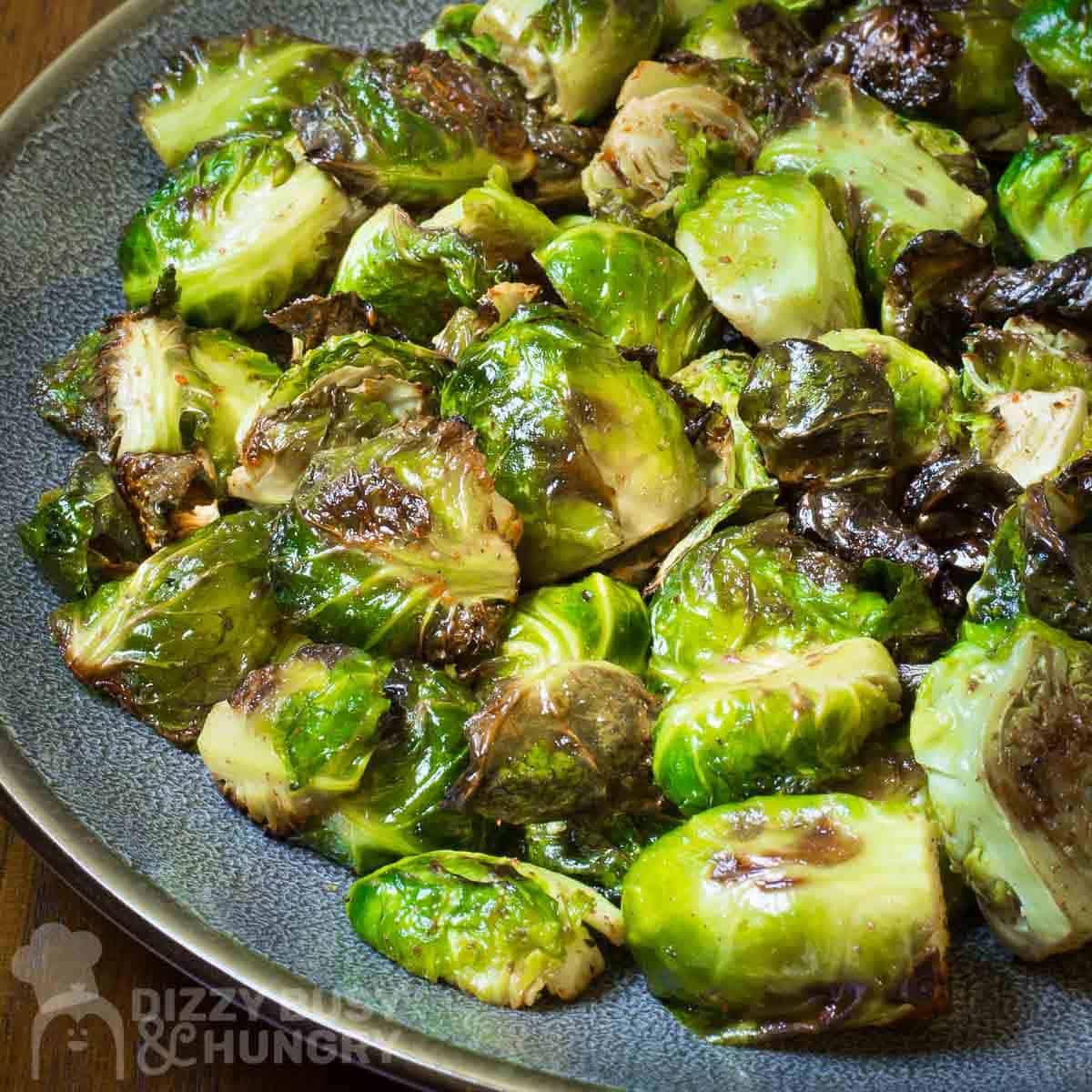 Side angled shot of garlic roasted Brussel sprouts on a blue and grey plate.