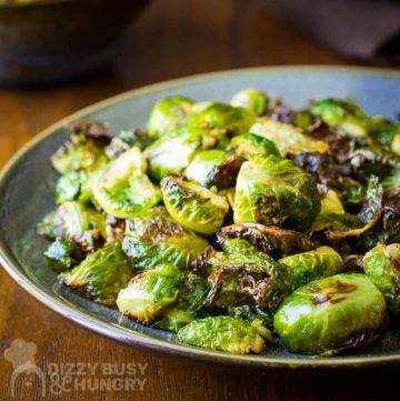 Side shot of garlic roasted Brussel sprouts on a blue and grey plate on a wooden table.