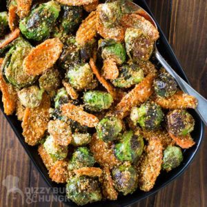 Overhead shot of roasted Brussel sprouts and carrots on a black plate on a dark wooden surface with a spoon on the side.