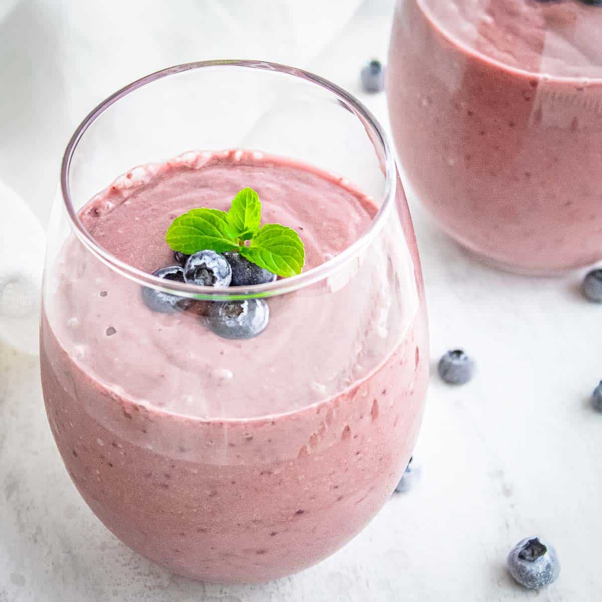 Side close up shot of the acai smoothie garnished with blueberries and mint in a clear glass on a white surface.