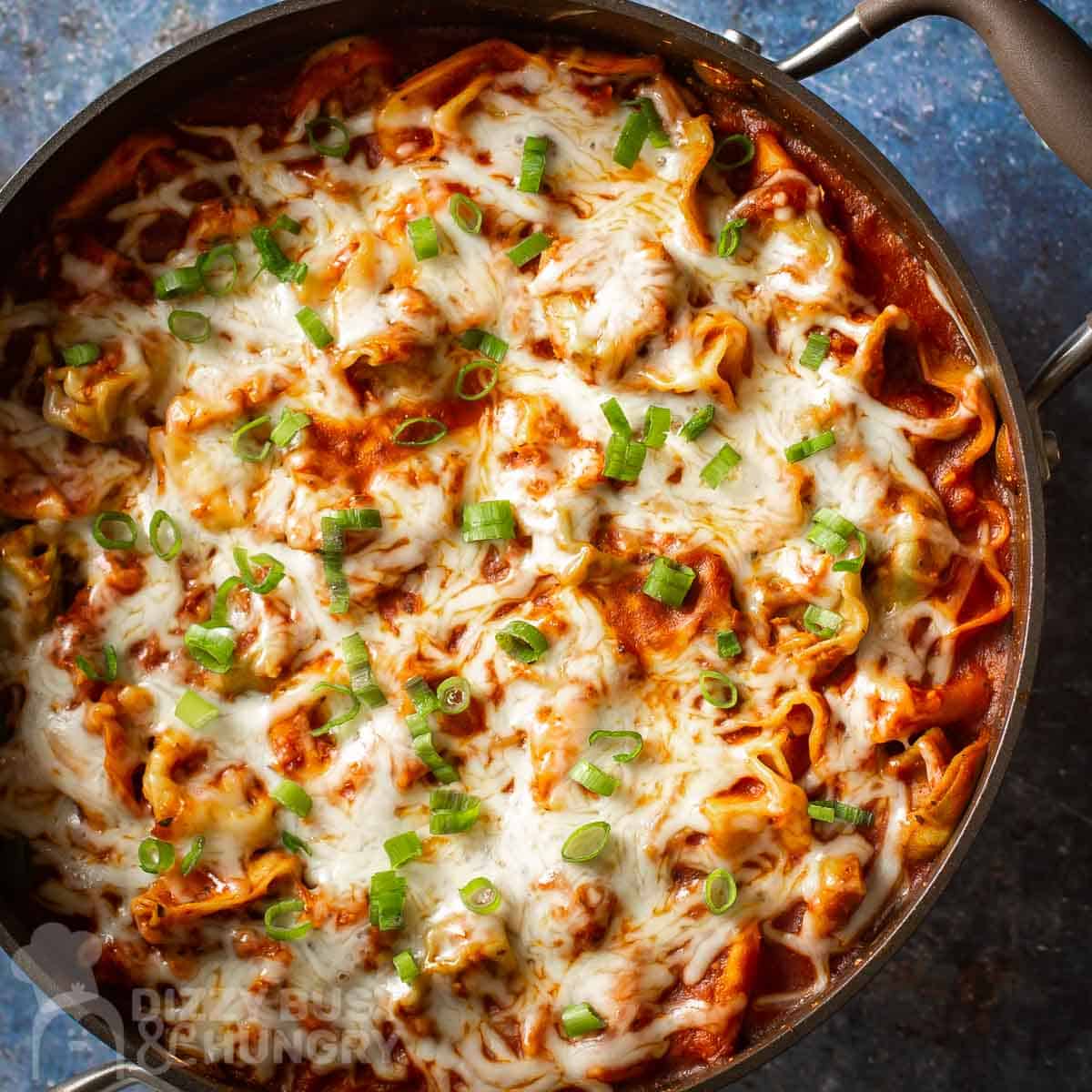 Overhead shot of cheese tortellini in a pot garnished with green onions on a blue speckled surface.