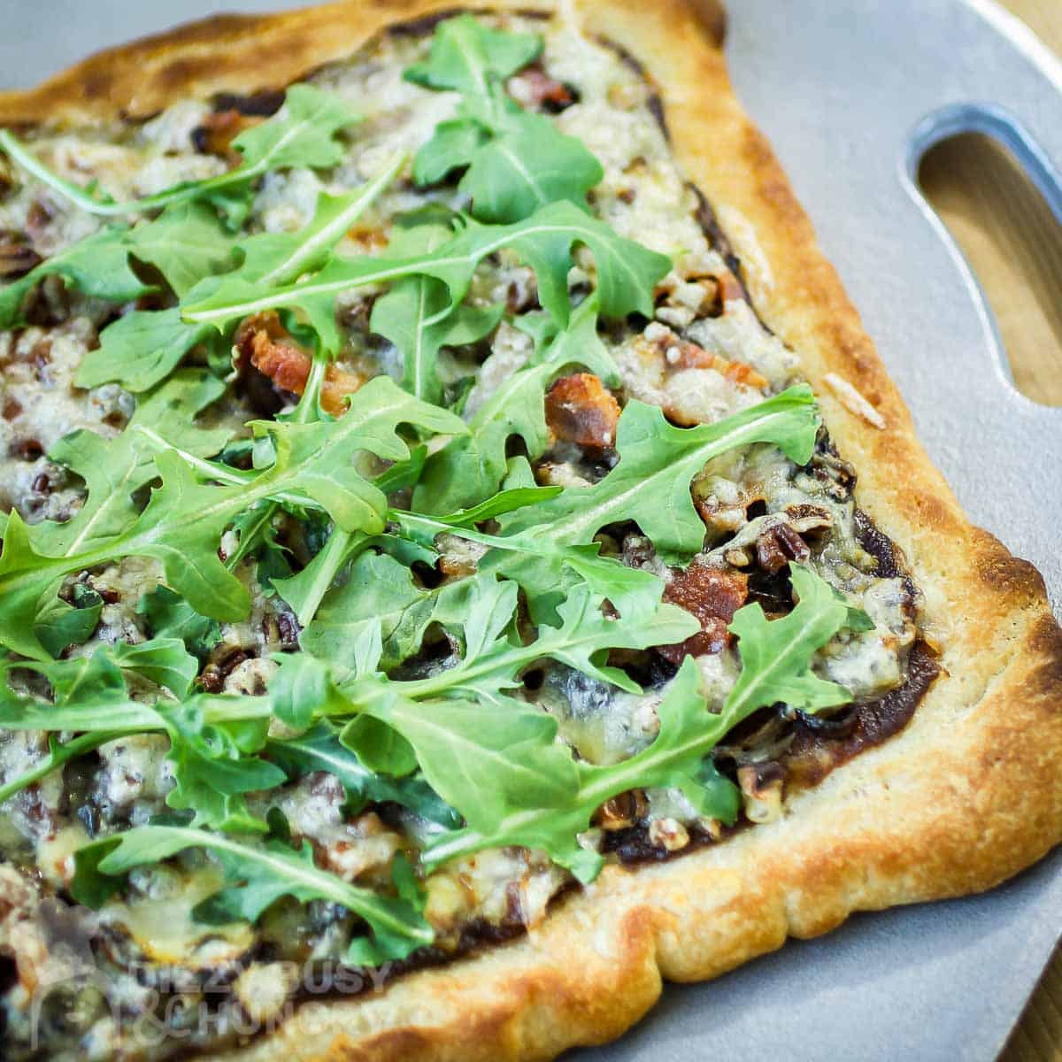 Side shot of the whole onion bacon pizza on a grey cutting board on a wooden surface.