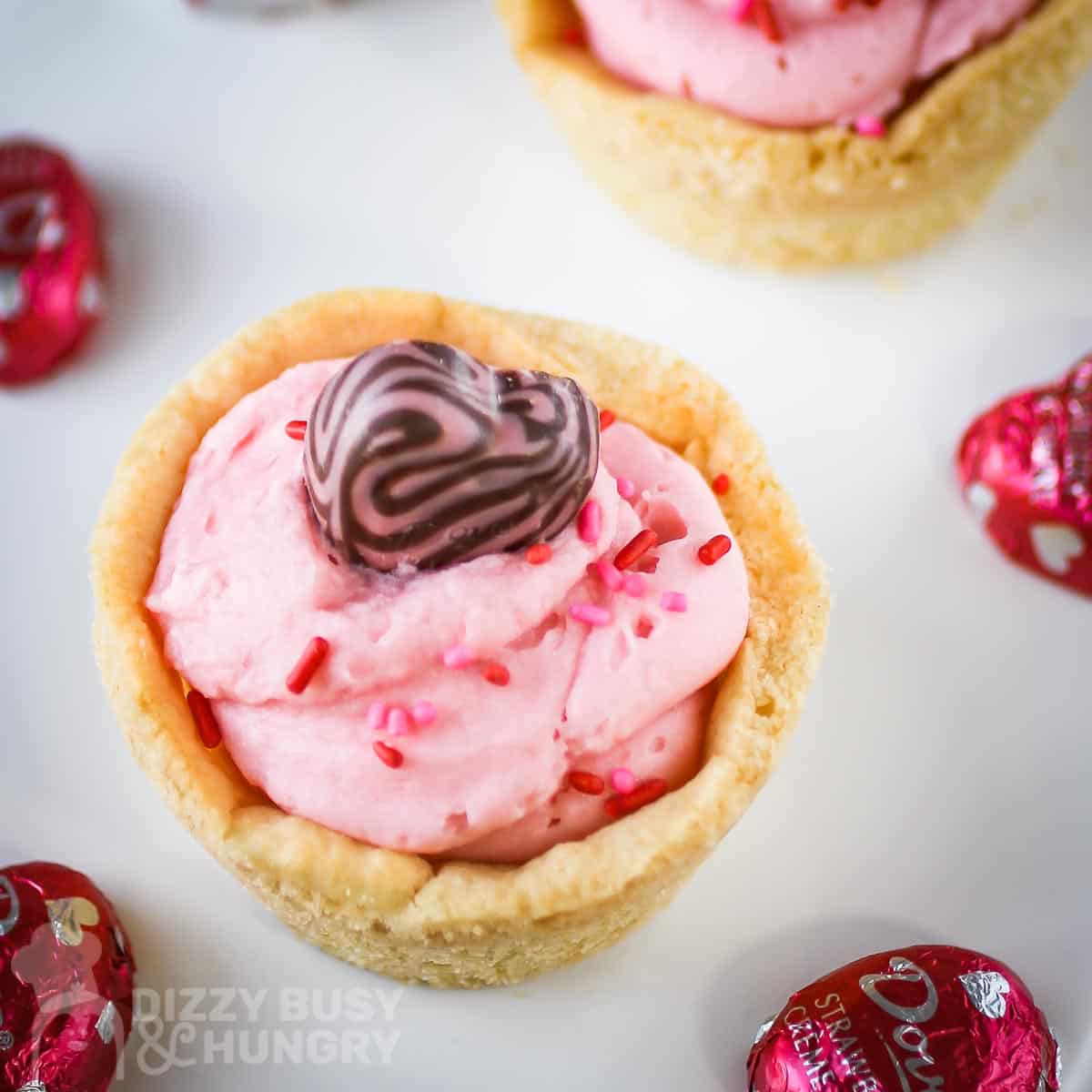 Close up overhead shot of two cookie cups on a white plate with pink chocolate hearts scattered around.