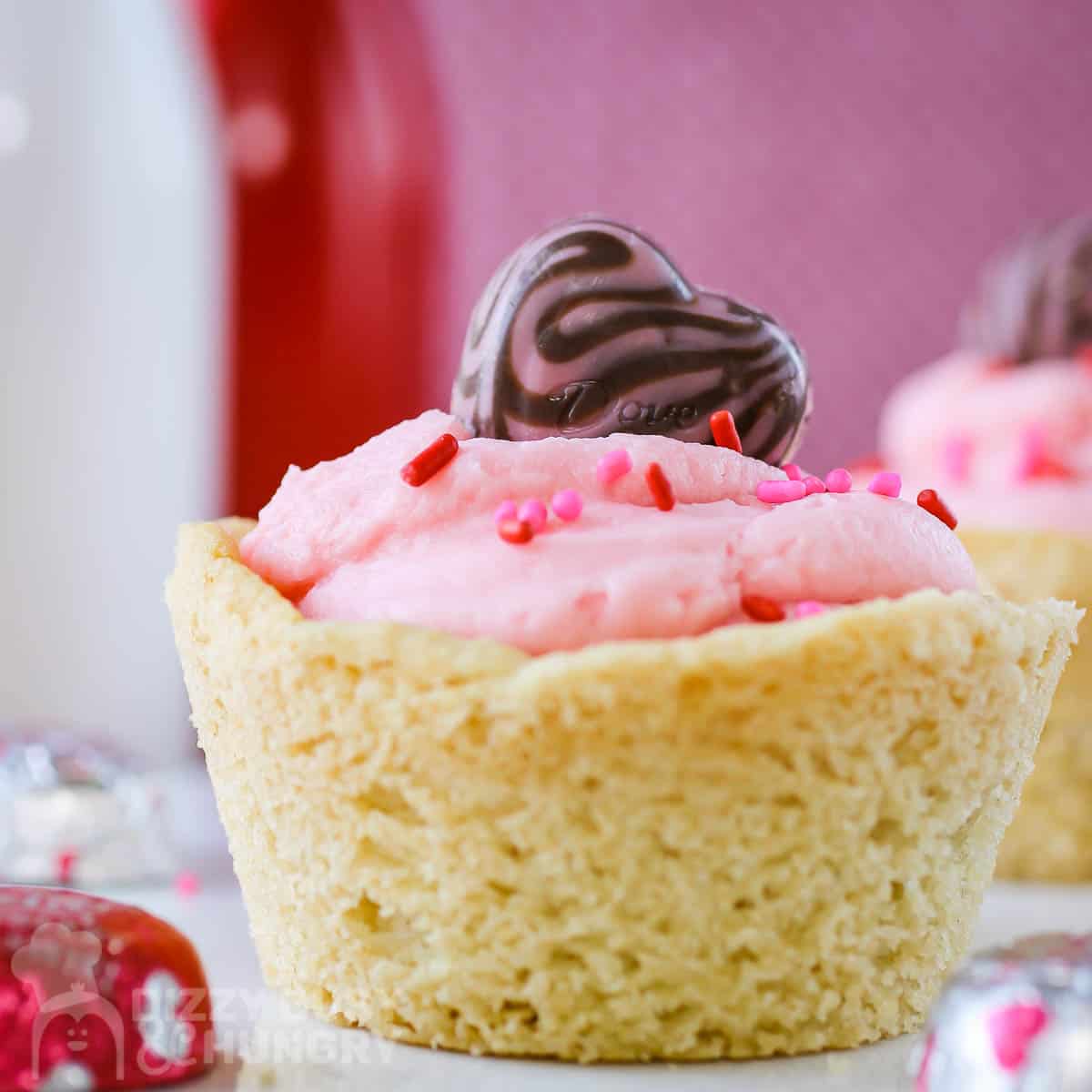 Close up shot of a cookie cup on a white plate with chocolate hearts scattered around with a pink background.