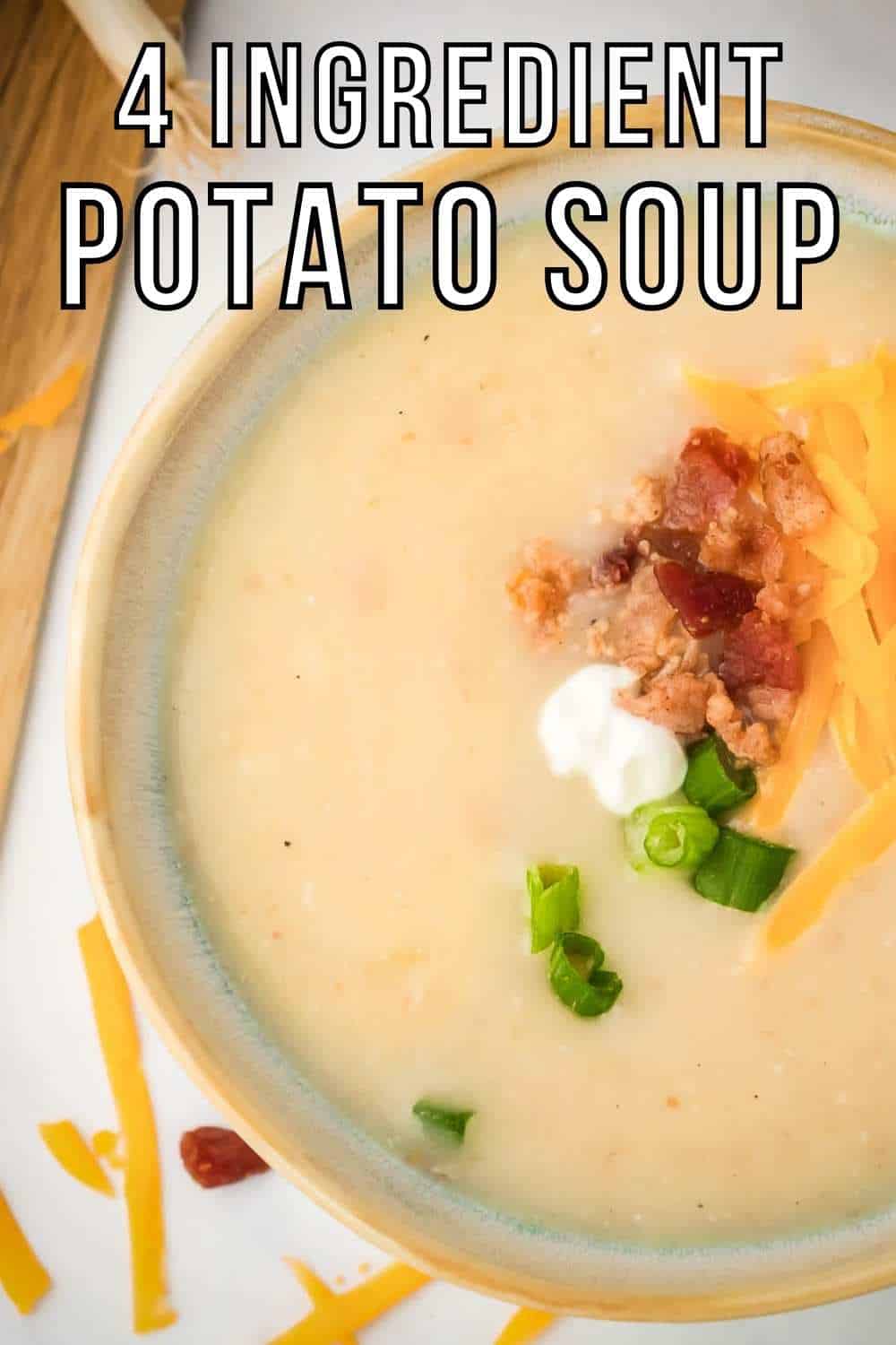 Close up overhead shot of potato soup garnished with shredded cheese, bacon, chives, and sour cream on a white surface.